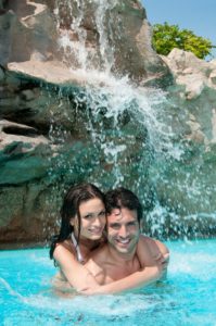 Couple in pool by large rock waterfall, Dreamscape by MGR leading pool contractor in Orange County